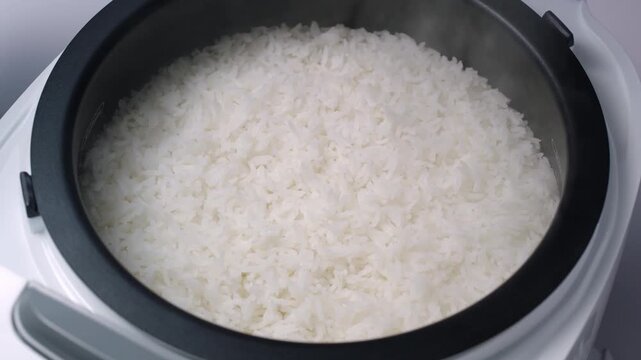 closeup hand putting hot cooked rice.close-up of freshly cooked, fluffy white rice inside a dark-colored pot, which is likely a rice cooker. A wooden rice paddle or spoon is resting partially buried	
