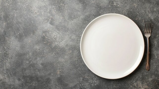 Overhead view of a minimalist table setting with an empty white plate and metal fork on a textured dark background offering ample copy space for food advertising