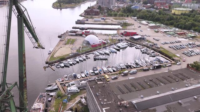 High-angle aerial drone footage showcasing a bustling coastal marina filled with docked yachts, a historic shipyard crane, and industrial port infrastructure tailored for maritime trade and tourism pr
