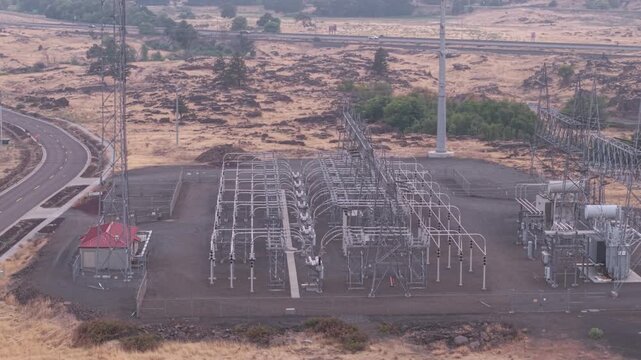 Electrical substation near a data center in The Dalles, Oregon, with Interstate 84 visible in the distance across the dry industrial landscape. Drone tilt-up shot.