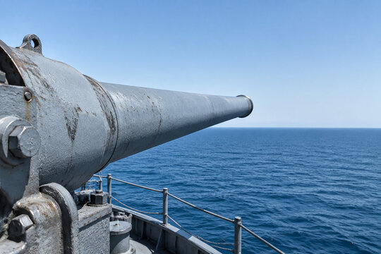 Close-up of a historic naval gun barrel pointing towards an empty ocean horizon.