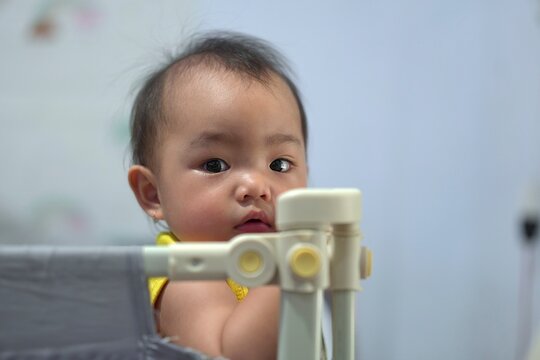 Close up portrait of a curious Asian toddler looking at camera from a playpen