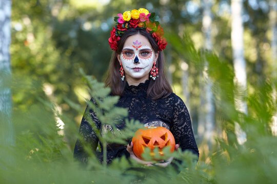 Halloween beauty portrait of female among ferns in the forest with Halloween pumpkin in hand.
