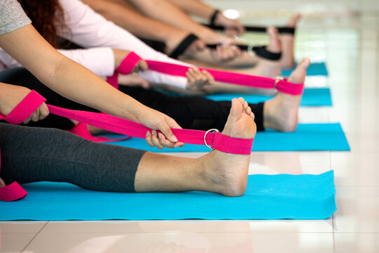 People performing seated yoga stretching with resistance straps on blue mats, improving flexibility, mobility, fitness, balance, strength, wellness, and group exercise indoors