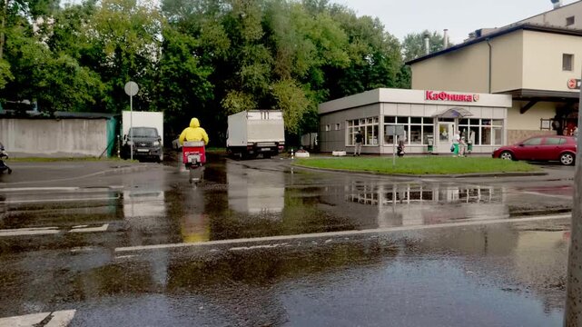 Delivery courier riding moped scooter on wet city street after rain with asphalt reflections