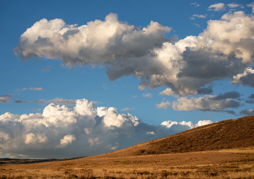 Dramatic cumulus clouds over rolling hills landscape in late afternoon light in  Wyoming