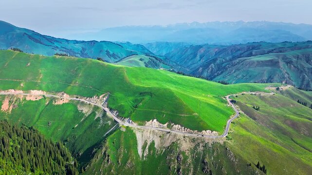 Aerial view of winding mountain road crossing green highland and rolling hills on Duku Highway, Xinjiang, China.