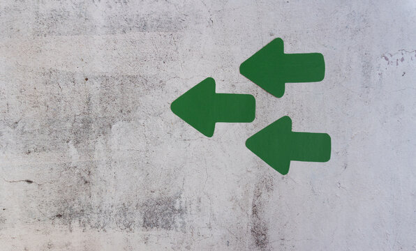 Green directional arrows painted on rough concrete surface