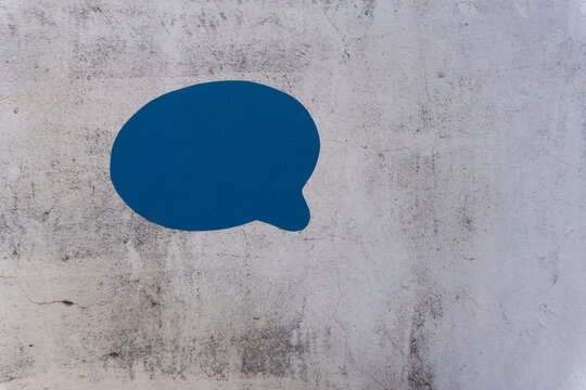 Blue speech bubble painted on rough concrete wall. Simple, modern graphic design. Ideal for communication, messaging, or chat themes.