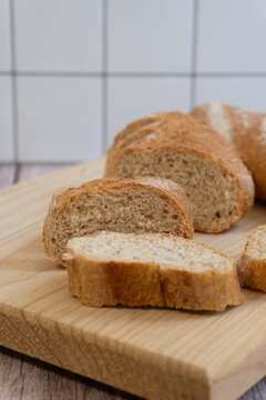 Freshly sliced artisan bread rests on a wooden board. Golden crust contrasts with soft, porous crumb inside. Background tiles add clean, minimalist kitchen context. Inviting texture suggests warmth