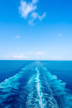 Water wake trail left by cruise ship in deep blue ocean under clear sky with copy space