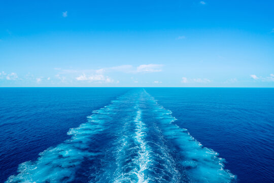 Water wake trail left by cruise ship in deep blue ocean under clear sky with copy space