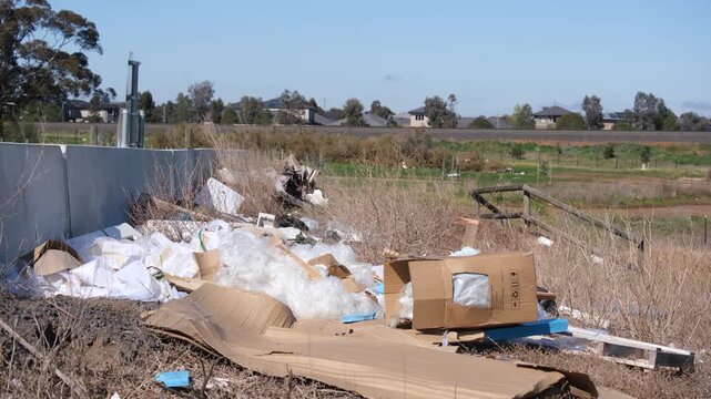 Illegally dumped&nbsp;waste, cardboard boxes, plastic packaging, and&nbsp;debris&nbsp;on a vacant peri-urban road reserve bordering new residential housing estates. Truganina, Melbourne, Victoria, Australia.