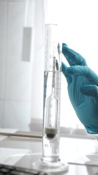 Close-up of a laboratory worker using a hydrometer in a graduated cylinder to measure liquid density during scientific testing and quality control.