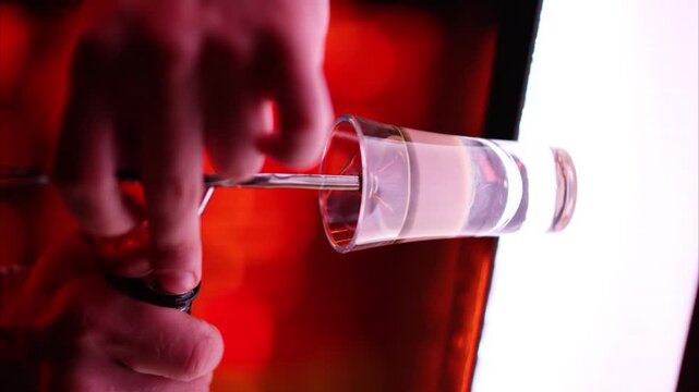 Bartender skillfully layering different colored liquids to create a vibrant shot glass cocktail in motion.