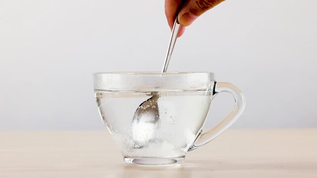 Stirring and Dissolving White Sugar in Glass Cup of Hot Water