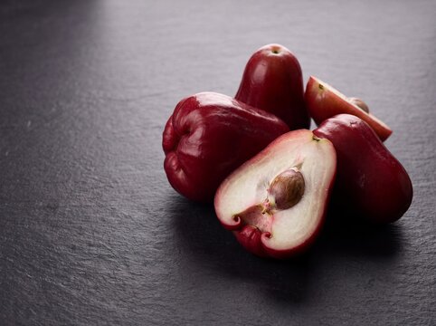Fresh jambu darsono Malay apple whole and halved showing seed on dark background
