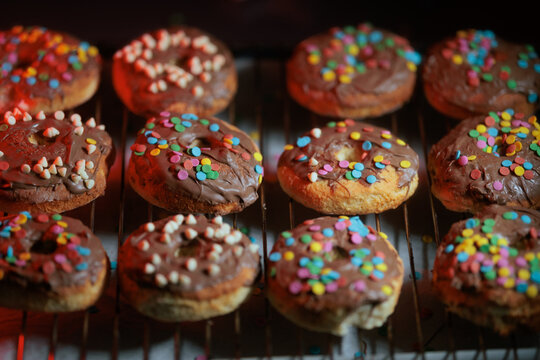 Homemade Healthy Baked Chocolate Glazed Doughnuts Decorated With Colorful Sprinkles. Delicious nutritious pastries covered in rich sweet frosting resting on wire cooling rack
