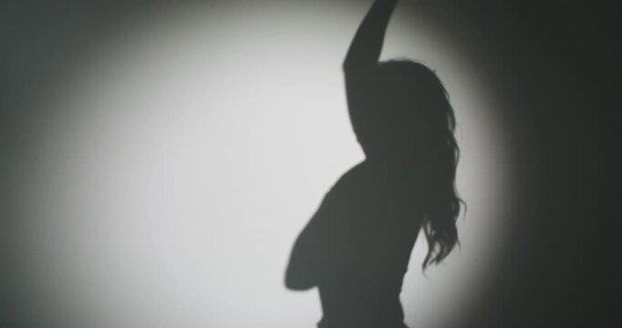 Woman silhouette. Projector light portrait. Model black shadow posing on white wall background in spotlight ray with sensual mood.