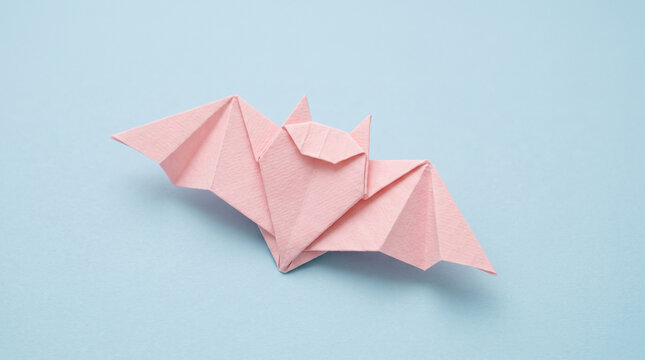Small pastel pink origami bat on a powder blue background with copy space, cute minimal halloween paper craft background