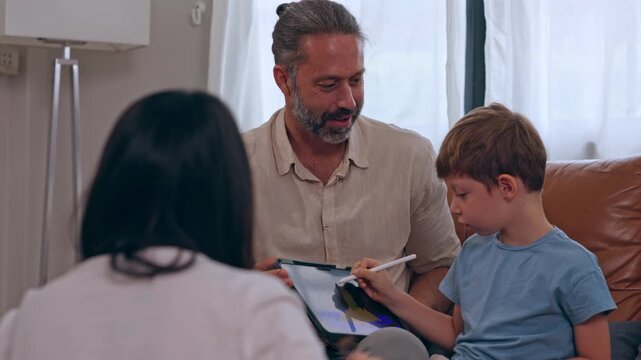 Father and boy drawing tablet home, caring parent supporting child during family healthcare moment, adult male sharing paper review and warm learning connection near bright window with mother nearby