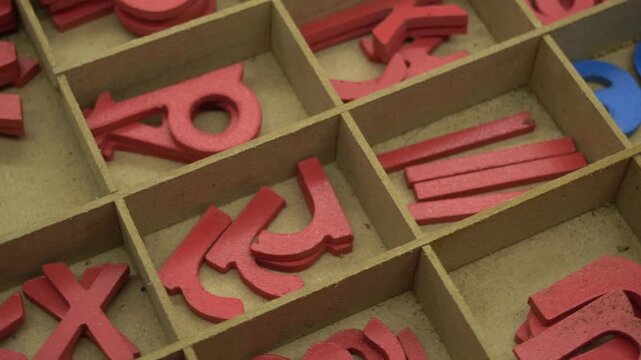 A rotating wooden tray containing red and blue alphabet letters for early childhood education and spelling practice in a classroom setting with a focus on tactile learning for young students