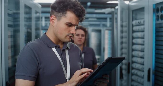 Standing in Server Room, Technician Analyzes Data Metrics on Tablet as Teammate Configures Server Rack Components. Mobile Diagnostic Tools and Physical Maintenance Optimize Cloud Server Efficiency.