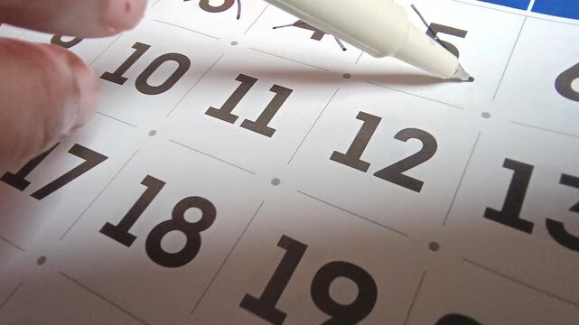 Close up view of person marking off dates on paper calendar with pen, time management and scheduling concept