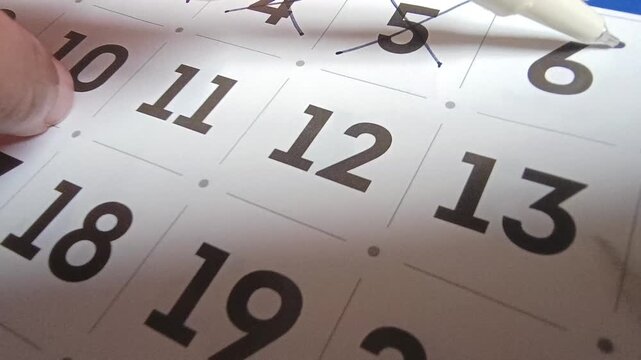 Close up view of person marking off dates on paper calendar with pen, time management and scheduling concept