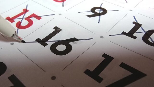 Close up view of person marking off dates on paper calendar with pen, time management and scheduling concept