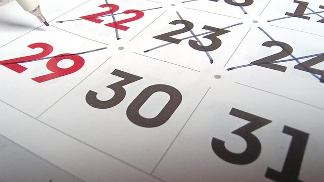 Close up view of person marking off dates on paper calendar with pen, time management and scheduling concept