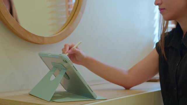 Close up of a woman hand using a pen with a digital tablet while working in the living room, modern technology, remote work, productivity, and home office lifestyle concept.