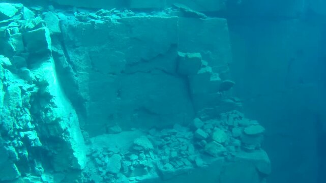 Panoramic underwater footage of a dramatic limestone rock wall inside a flooded quarry. The camera smoothly pans across rugged cliffs and broken rock formations.