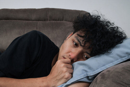 Depressed Young Man Lying On Sofa Resting His Head On Pillow