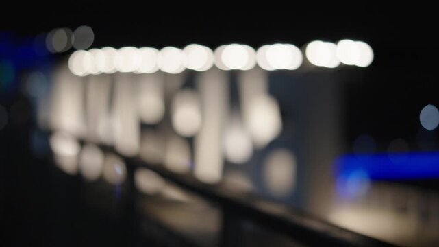 An abstract out-of-focus night scene showing bright white bokeh circles and elongated light shapes reflecting on surfaces near a dark bridge.