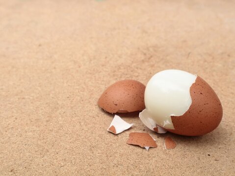 Close up of a partially peeled hard boiled brown egg with shell fragments on a wooden background. Ideal for healthy diet, breakfast nutrition, cooking recipes, and high-protein snack concepts