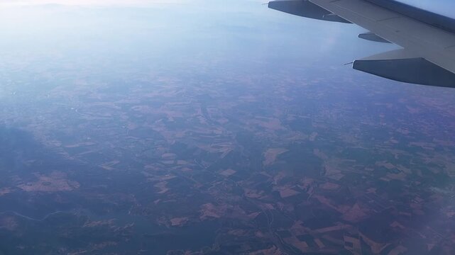 Aerial view from airplane window showing patchwork agricultural fields and rural landscape below with aircraft wing visible