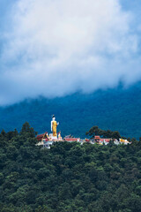 Obraz premium Standing Buddha Statue at Wat Phra That Doi Kham Temple, Chiang Mai, with Misty Mountain Landscape