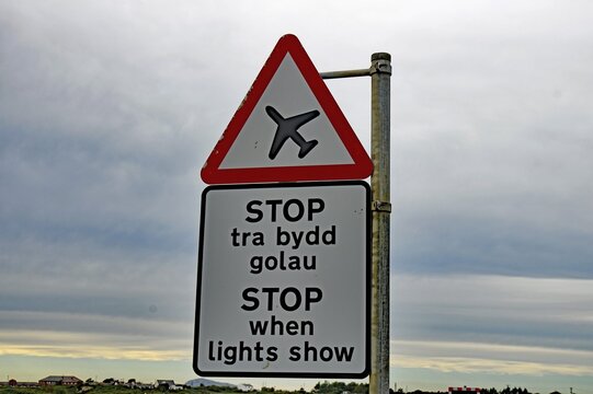 Road sign with an aeroplane symbol and bilingual text in a rural landscape under a cloudy sky, Shetland Islands, Scotland, United Kingdom