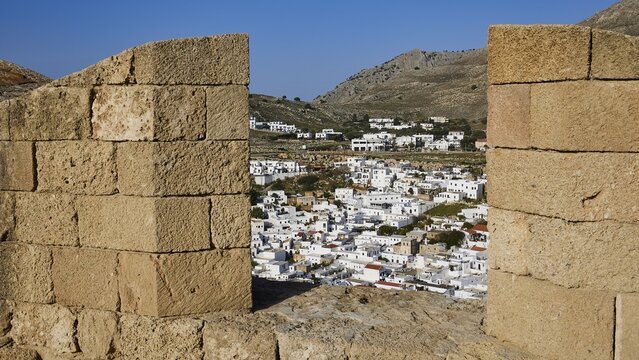 View through an old stone wall to a settlement with white houses and mountains in the background, St John's Fortress, Lindos, Rhodes, Dodecanese, Greek Islands, Greece