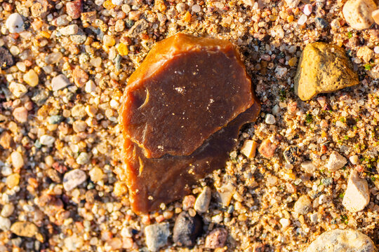 Close-up of a raw amber-colored flint stone resting on textured sandy ground, showcasing sharp edges and natural geological patterns in warm golden sunset light