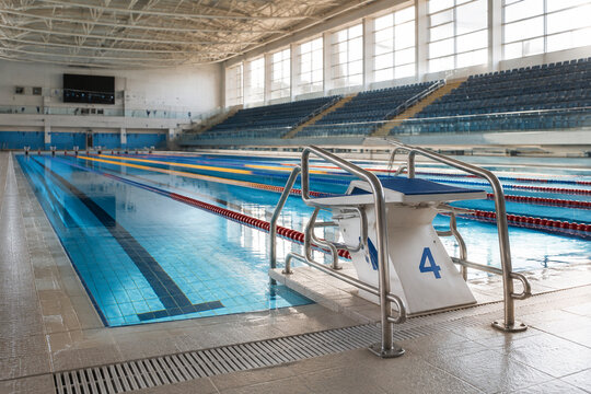 An empty swimming pool arena with a starting block and assistive handrails.