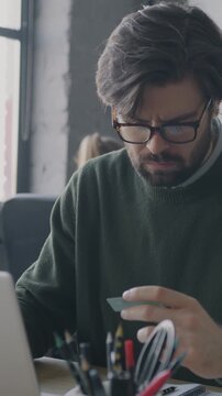 Young businessman using laptop computer holding credit card smiling using electronic money in office. Banking and finance concept.