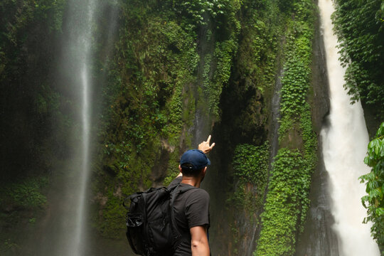 Traveler points at a waterfall amid lush greenery in Bali