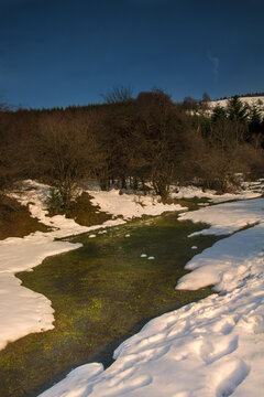 Winter landscape of the Otzarreta beech forest covered in snow with a small stream flowing through the iconic pollard trees in Gorbea Natural Park