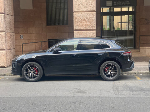 A modern black Porsche Macan SUV is parked curbside on a paved urban street, showcasing its sporty design and alloy wheels