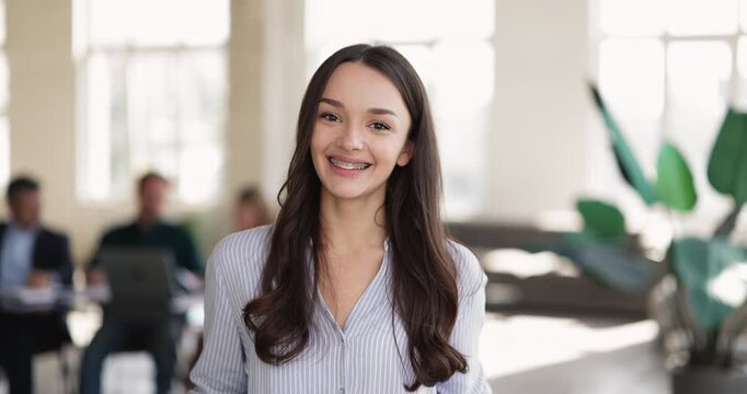 Headshot portrait motivated young female intern smiling at camera with enthusiasm confidence enjoying start of professional career in modern office proud of getting first job joining corporate team