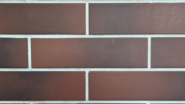 A close-up view of a modern brown brick wall featuring clean white mortar joints in a running bond pattern.