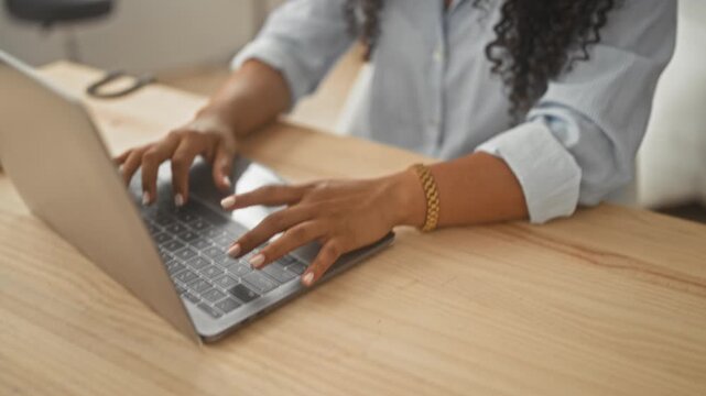 Woman typing on laptop with hands on keyboard and wearing bracelet, looking down in bedroom; calm productivity focus.