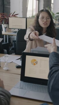 Businesswoman team leader handing out documents talking to employees at meeting in office. Professional gathering and workplace concept.